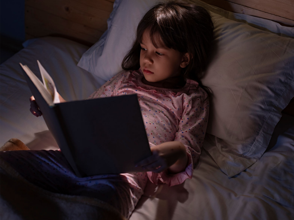 A girl is reading a pre-loved book lying on her bed.